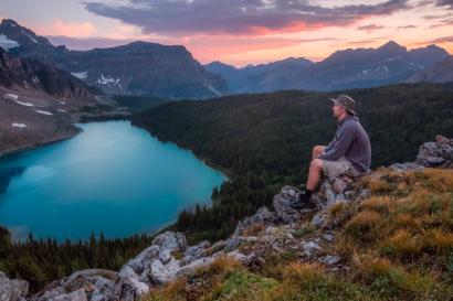 a man sits on a rock overlooking a lake at sunset