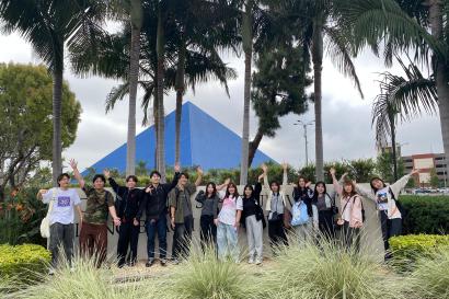 Group of students on the CSULB campus with palm trees and the Walter Pyramid Stadium in the background.