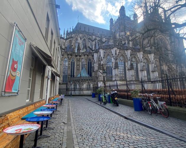 A side view of the cathedral next to a stone street with a restaurant on the left hand side. There are places you can sit outside the restaurant to see the cathedral.