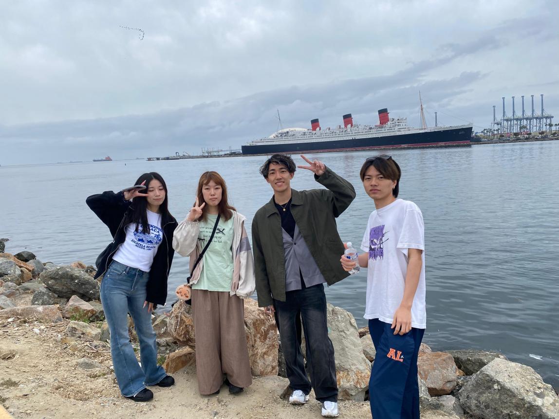 Four students posing by the ocean, with a big ship in the background.