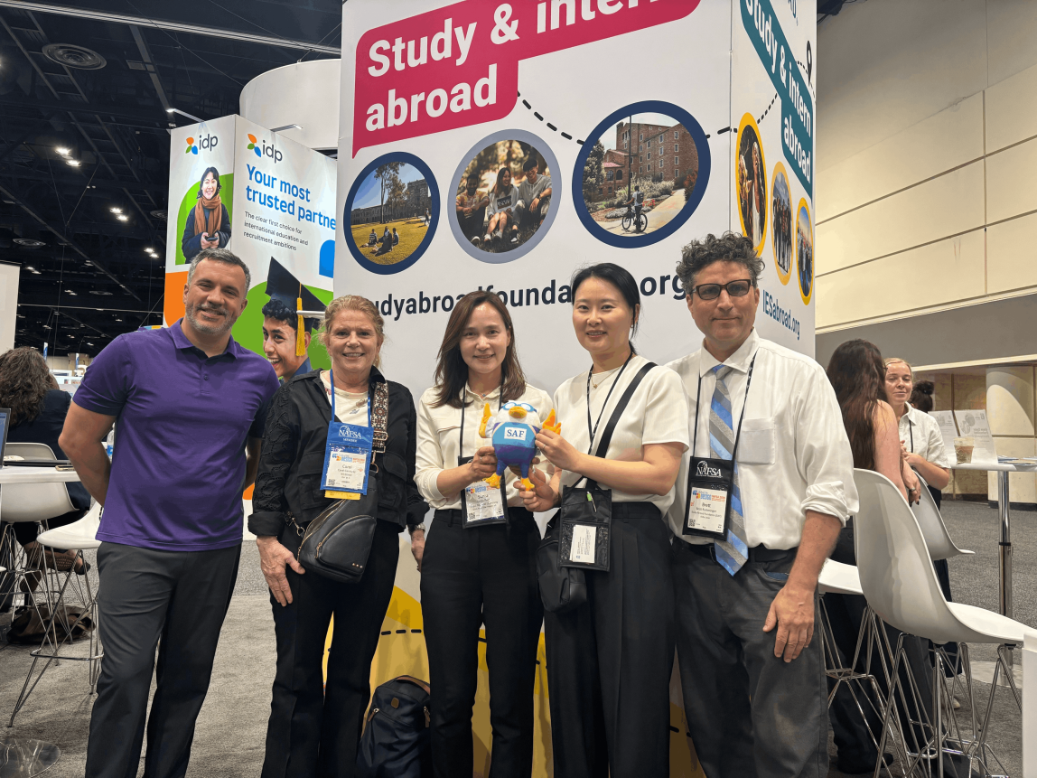 SAF Leadership pose in front of the IES Global booth with a university partner and SAFFY doll at NAFSA 2026.