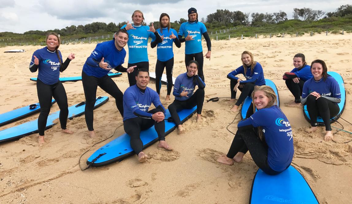a group of students pose for a photo with their surf boards and surf gear on the beach in Sydney