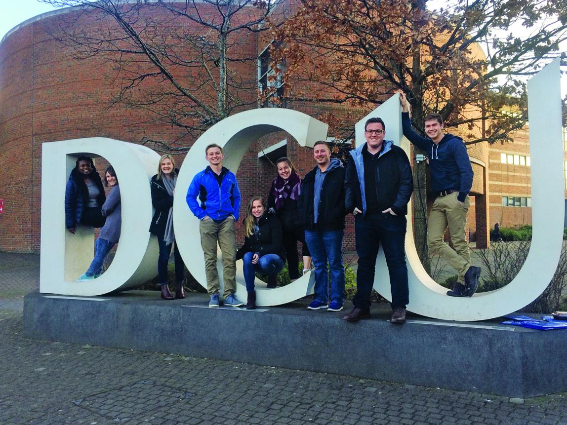 Students stand on Dublin City University's giant letter display. The letters are "DCU."