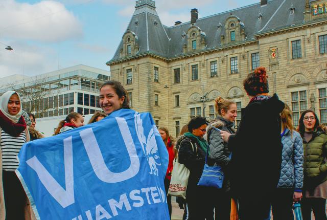 Students celebrating outside on Vrije Universiteit's campus. One student is wearing a blue VU flag.
