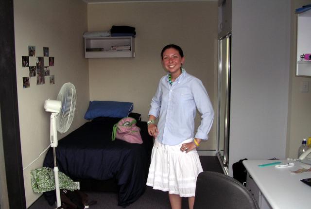 A student stands in their UNSW Shalom College student room, with a bed, a desk, and a bathroom.