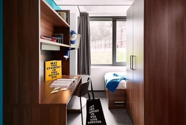 student apartment in amsterdam with wooden furniture including a desk, bed, and tall windows