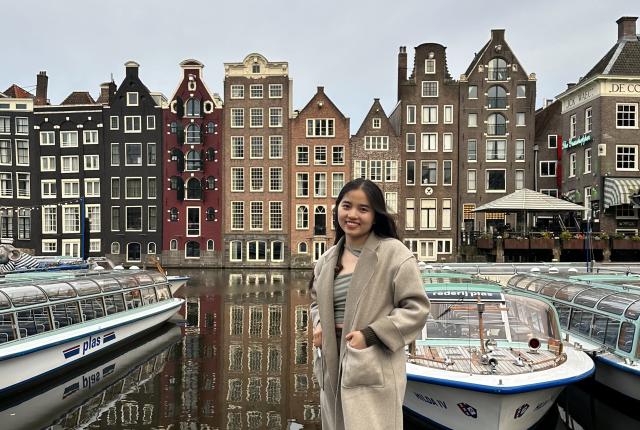 Student standing in front of Boats and Rows of Houses in Amsterdam Canal