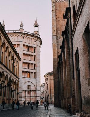 People walk in the historic center of Parma. The buildings are made of red brick and some have spires atop them.