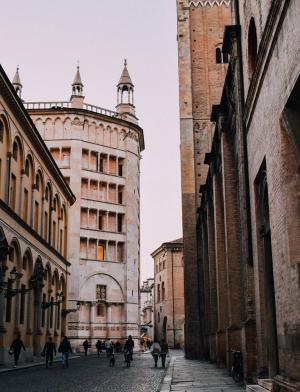 People walk in the historic center of Parma. The buildings are made of red brick and some have spires atop them.