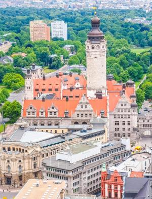 A top down photograph of Leipzig. There are numerous bustling streets, buildings, and a tall clocktower in the center of town.