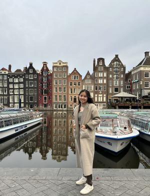 Student standing in front of Boats and Rows of Houses in Amsterdam Canal