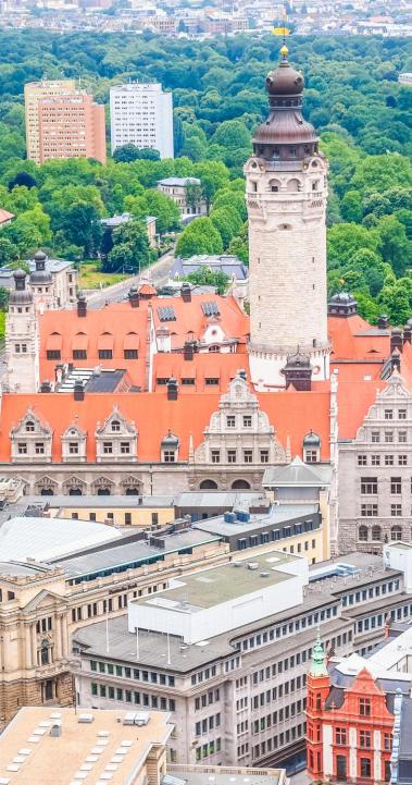 A top down photograph of Leipzig. There are numerous bustling streets, buildings, and a tall clocktower in the center of town.