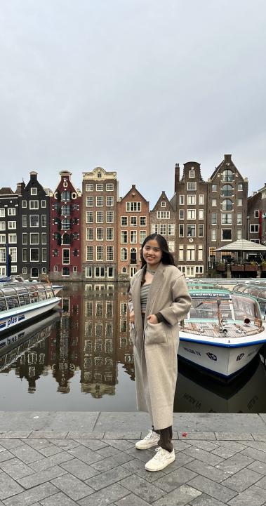 Student standing in front of Boats and Rows of Houses in Amsterdam Canal