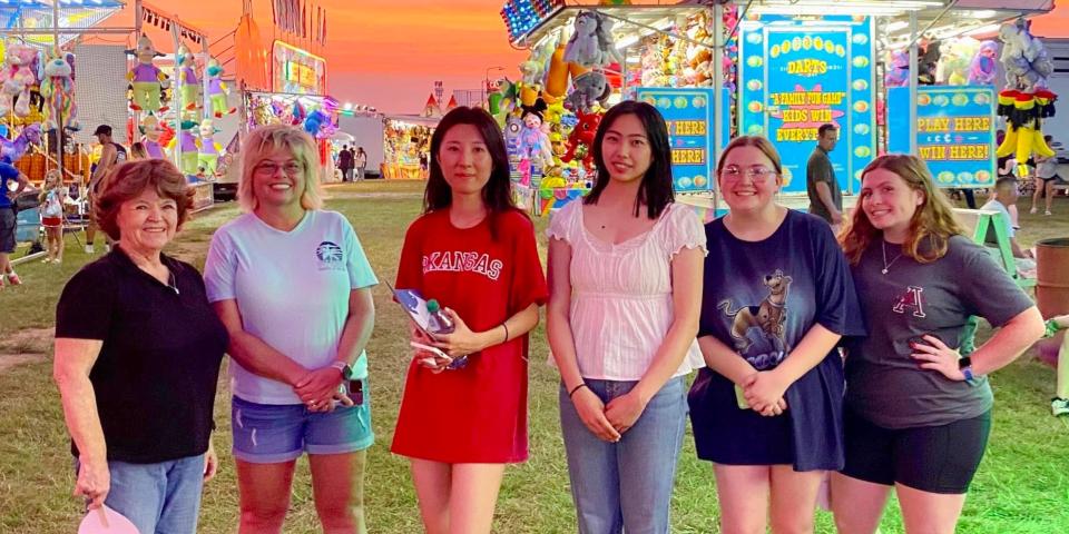 アメリカ、アーカンソー大学のイベントでホストファミリーと友人たちと遊園地へ。背後にはオレンジ色の美しい夕焼けと様々な出店。
